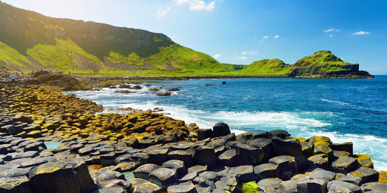 Panoramic view of the unique hexagonal basalt columns stepping into the ocean under a clear blue sky at Giant's Causeway in 2026